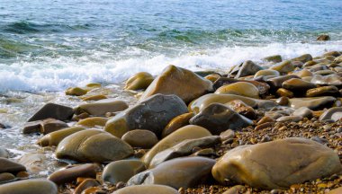 Taşlı sahilde yuvarlanan deniz dalgaları, yakın bir yerde