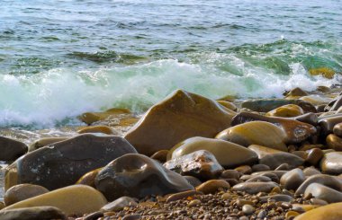 Taşlı sahilde yuvarlanan deniz dalgaları, yakın bir yerde