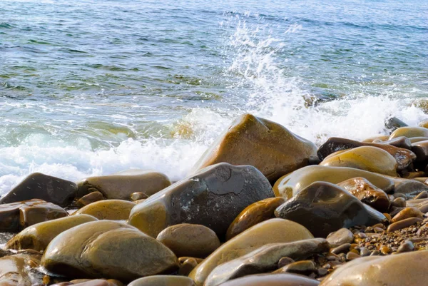 Taşlı sahilde yuvarlanan deniz dalgaları, yakın bir yerde