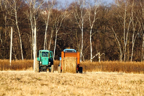 Tractores para la cosecha de hierba seca en fardos de paja en un campo en el otoño. Equipo agrícola especial. Profundidad superficial del campo . —  Fotos de Stock