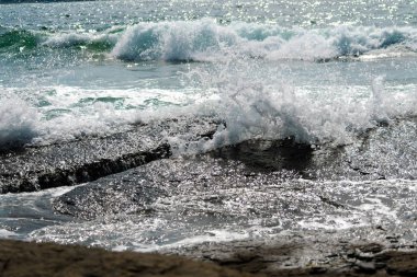 Taşlı sahilde yuvarlanan deniz dalgaları, yakın bir yerde