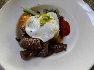 Kalbi Loco Moco yumurta üzerinde kolay, pirinç, kim chee ve beyaz tabakta sıcak sos ile.