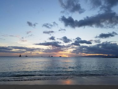 Bulutlar üzerinde günbatımı ve Oahu sahilinde tekneler ile su üzerinde Pasifik Okyanusu yansıtan, Waianae dağ aralığı ile Hawaii görünür.