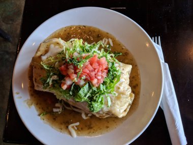 Nihai Cali Burrito ile beyaz bir plaka üzerinde yeşil Şili sos, peynir, tettuce ve pico de gallo 'çözümlemen-style' boğdu.