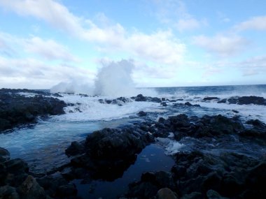 Wave crashes over Tide pools filled with water on lava rock shore with ocean on the horizon at Makapuu point on Oahu, Hawaii. 2015. clipart