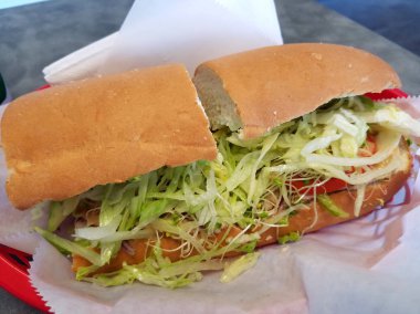 Balmumu kağıt peçete ile taze alt sandviç. Marul, peynir, domates, avakado, hardal ve masada ekmek.