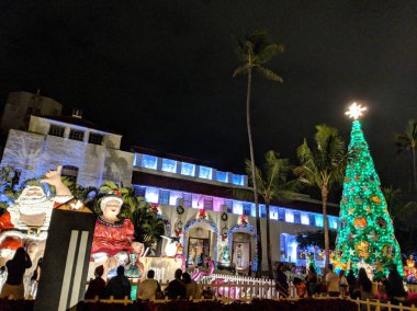 Honolulu - 18 Aralık 2017: Hindistan cevizi içki, POI çanta ve Lau lau ışık tutan kaplumbağa rakam ile üst şelale ve yılbaşı ağacı yıldız Bay ve Bayan Noel oturup gece Honolulu Hale, Belediye Başkanı ofis önünde insanlar göz, 