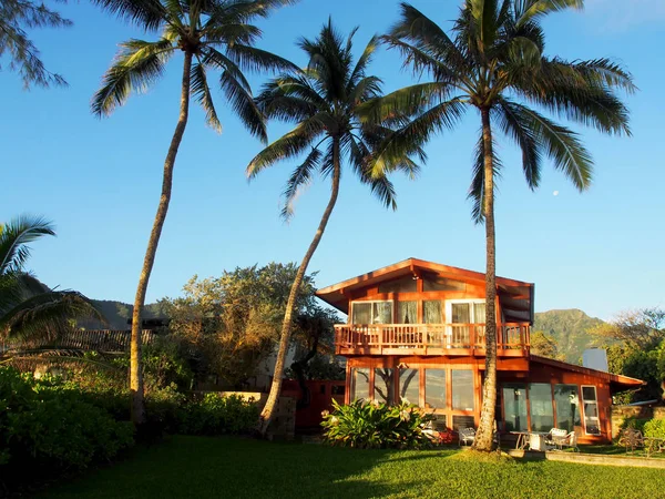 Red Beach House in Waimanalo with moon in blue sky and mountains in the distance on a Beautiful Day on Oahu, Hawaii.