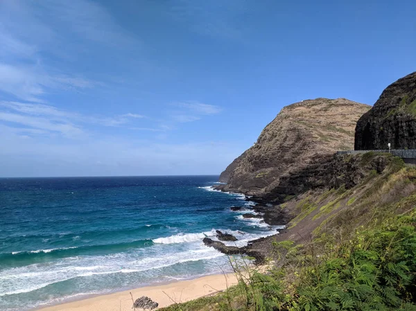 Wave break at Makapuu Beach with Lighthouse in on mountain cliff in the distance on a nice day on Oahu, Hawaii.
