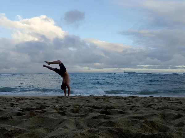 Człowiek robi Handstand na plaży o zachodzie słońca, jak fala katastrofy — Zdjęcie stockowe