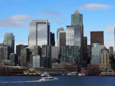 18 Mayıs 2019 - Seattle, WA: Seattle şehir merkezindeki binalar, Piers ve Puget Sound 'un önündeki su boyunca yarışan teknenin su manzarası.