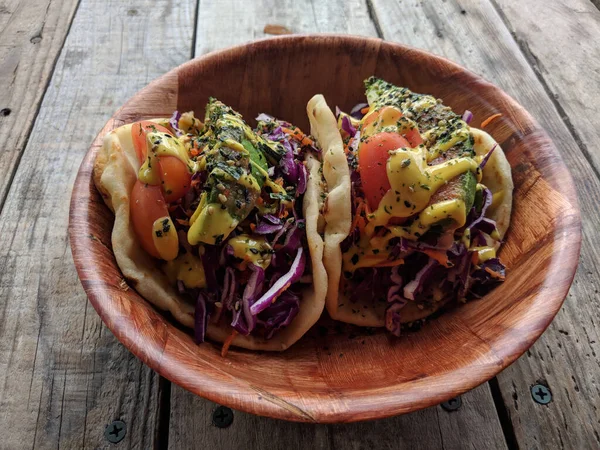 Rainbow Tacos: Veggie mix of red cabbage, green onion, carrot, and Japanese cucumbers.  Served on warm naan with hummus and balsamic drizzle. Topped with avocado, grape tomato, and almonds.