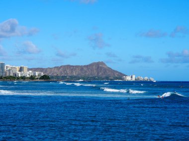 Honolulu - 13 Ağustos 2017: İnsanlar güzel bir günde Oahu, Hawaii 'de Hindistan cevizi ağaçları, apartman binaları, bulutlar ve elmas başlıklı kraterle birlikte Kewalo Havzası Parkı' nda suda sörf yapıyor..