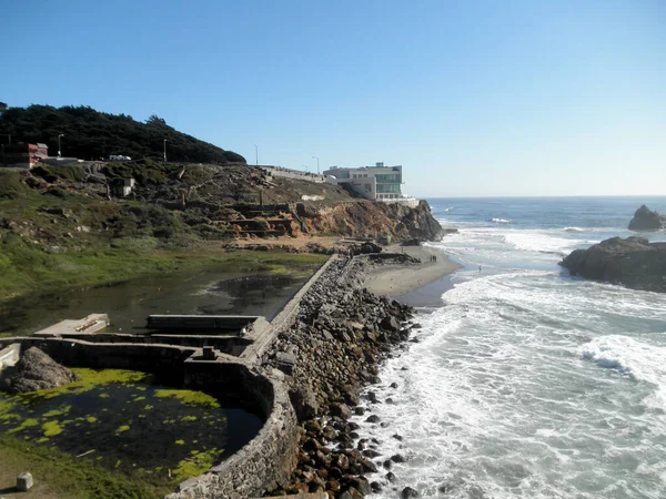 Waves roll towards shore of Ocean Beach with Cliff House and the ruins of the Sutro Bath House in foreground in San Francisco, California.