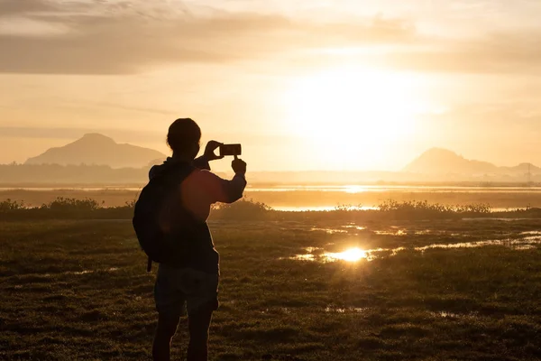 Sylwetka kobiety trzymając smartfon fotografowanie poza podczas wschodu lub zachodu słońca. — Zdjęcie stockowe