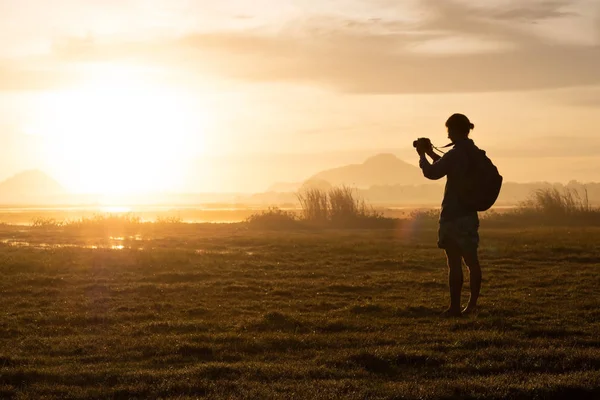 Sylwetka kobiety trzymając smartfon fotografowanie poza podczas wschodu lub zachodu słońca. — Zdjęcie stockowe