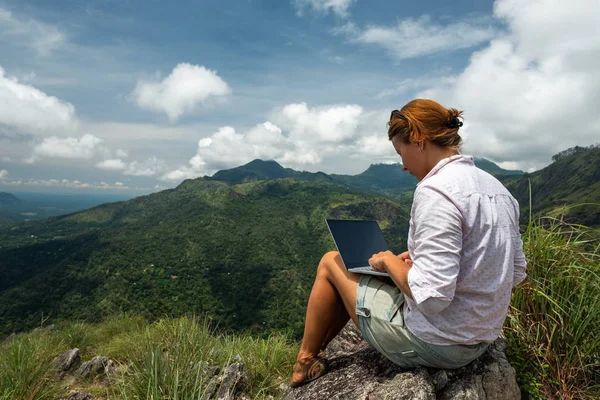 Girl working on her computer on the top of the mountain.