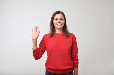 Avrupa Genç dostu görünümlü elini sallayarak Selam, kırmızı pulover giyinmiş.