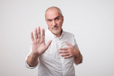 Mature man in white shirt showing sign stop with hand. Deny to do something clipart