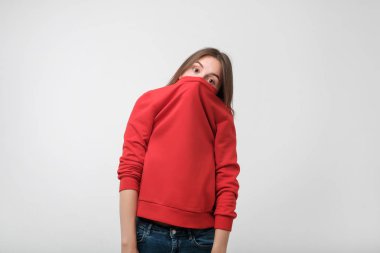 A girl with a social phobia hides her face in a sweater. She looks frightened at the camera clipart