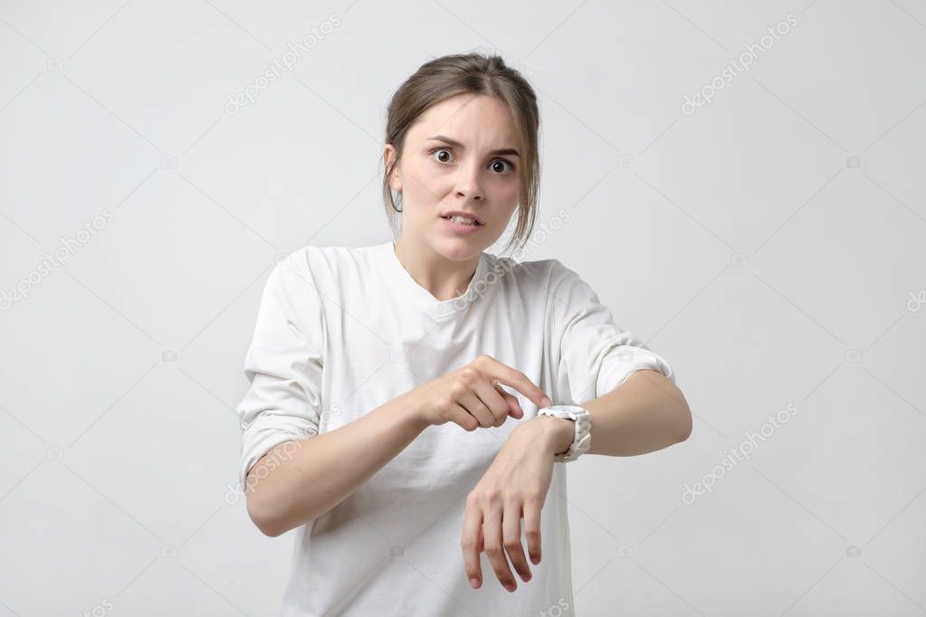 Young pretty caucasian student is angry because of being late. She is showing time on her watch. Concept of irritation of dead line.