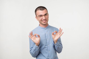 Genç latin yakışıklı bir adam gri arka plan üzerinde ok işaret gösteren izole mavi gömlekli. Başarı, zafer çalışmalar veya iş proje kavramı