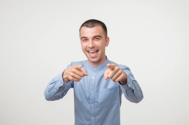 Mavi gömlekli neşeli genç adam kapalı atış, rekabet için seçtiği, pozitif ifadesi olan mutlu bir şekilde sana gösterir. Yakışıklı zeki öğrenci doğru bir seçim yapar