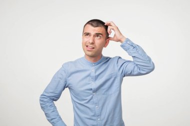 Çatık ve tırmalamak süre baş, tatminsiz seyir yakışıklı İspanyol çocuk mavi gömlekli gri arka plan üzerinde duruyor. O bazı gerçekleri ya da ne yapacağımı hatırlamıyorum. Hafıza ile ilgili sorunlar