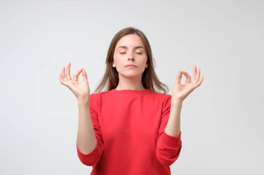 Gri arka planı ayakta zen hareketlerle eller yükselterek gülümseyen kırmızı gömlek içinde meditasyon sakin güzel beyaz kadın kapalı portresi. Sakin zihin için yoga sınıf kavramı