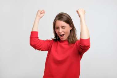 happy caucasian woman in red sweater exults pumping fists celebrates success or victory of her football teamShe has passed exam or receive new job clipart