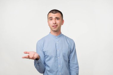 Young man in blue shirt standing disorientated bewildered isolated on gray wall background. Decision making concept. Human facial expression emotions clipart