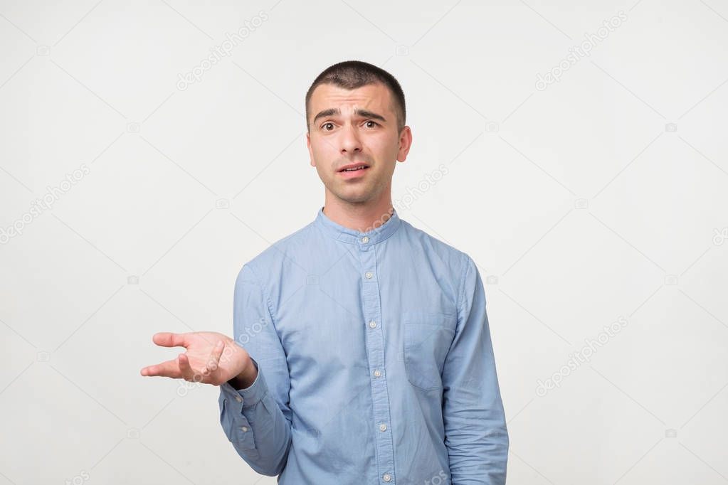 Young man in blue shirt standing disorientated bewildered isolated on gray wall background. Decision making concept. Human facial expression emotions