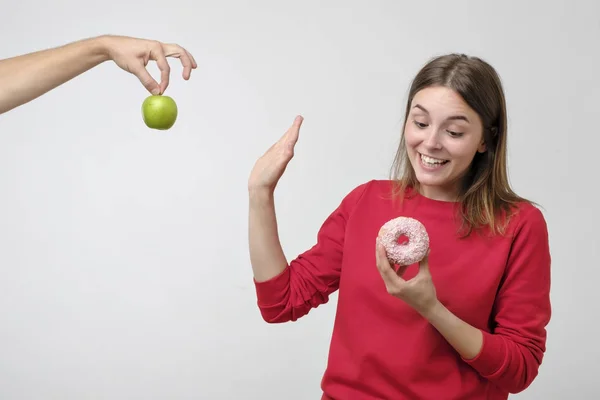 健康食品とダイエットのコンセプトです 美しい若い女性が果物とお菓子との間を選択します 彼女は緑のリンゴではなくピンク ドーナツを好む — ストック写真