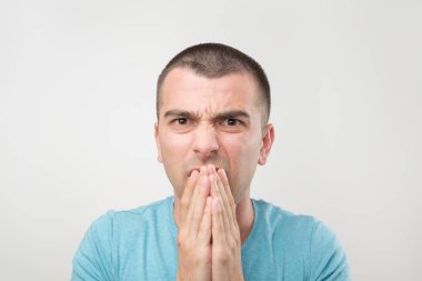 İğrenç yüz duygu. El ağzı kapatma ve çatık mavi t-shirt genç yakışıklı adam. O koku gibi değil ya da ne gördüğünü