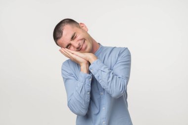 Genç adam onun avuç içi gibi bir yastık koyarak bir mavi gömlekli kıyafeti giymiş. Uykulu ve yorgun arıyorsunuz. Hiçbir enerji kavramı