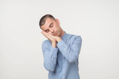 Genç adam onun avuç içi gibi bir yastık koyarak bir mavi gömlekli kıyafeti giymiş. Uykulu ve yorgun arıyorsunuz. Hiçbir enerji kavramı