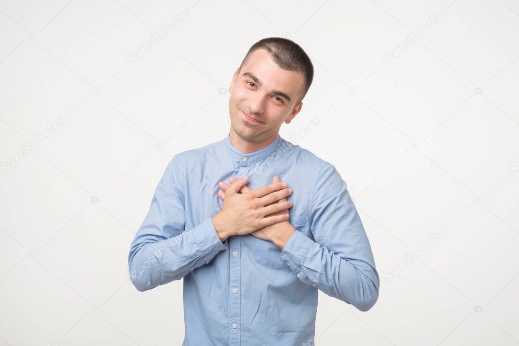 Kind spanish man in blue shirt with pleased expression looking into camera, keeps hands on heart, expresses his positive feelings towards girlfriend. Concept for saint Valentine day