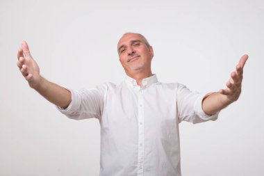 Hoş geldiniz kavramı vardır. Hoş geldiniz işareti işaret ve gri duvarın karşısında dururken gülümseyen Beyaz tişörtlü neşeli olgun adam. Sevgili misafirler karşılamak mutlu olduğunu