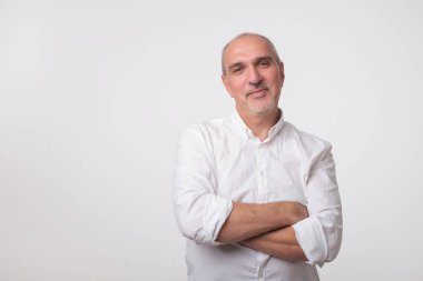 Elleri göğsünde geçiş ve gri arka plan karşı dururken kamera bakıyor beyaz t-shirt emin komuta sizde. Kendi kendine güvenen İspanyol kıdemli.