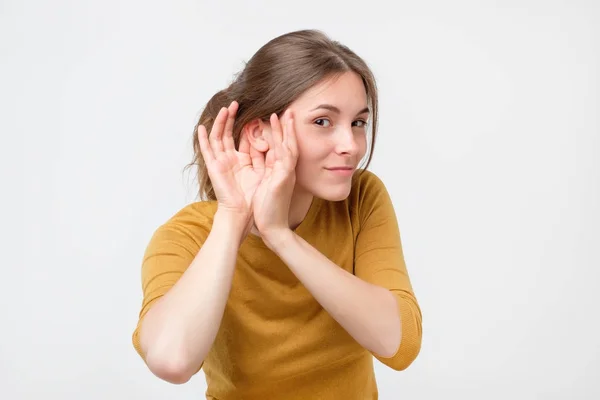 Молода жінка в жовтому светрі слухає плітки про інше з рукою біля вуха . — стокове фото