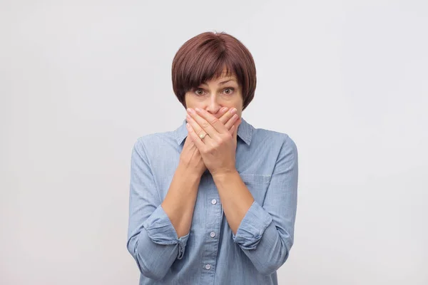 Primer plano retrato de mujer atractiva y madura en camisa azul cerrando la boca con los dedos. Está preocupada. . —  Fotos de Stock