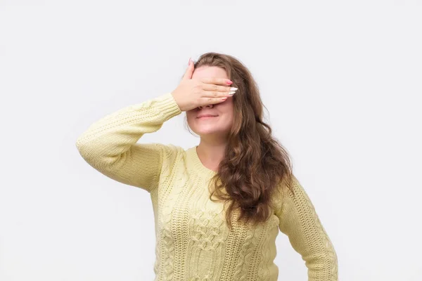 Menina europeia bonita em suéter amarelo fechando os olhos com a mão, tendo expressão feliz — Fotografia de Stock