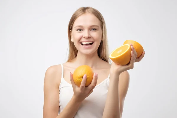 Schöne junge blonde Frau in weißem Hemd, die ein Stück Orange in der Nähe ihres Kopfes hält und lächelt — Stockfoto