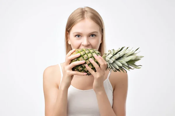 魅力的な若い女性の白い背景の上にパイナップルをかむ — ストック写真