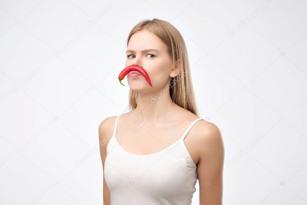 European young woman holding red hot chili pepper like mustache