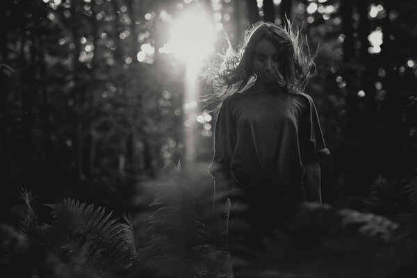 Monochrome photo of european woman standing alone in forest. Mystical mood and loneliness concept. Dust and noise effect