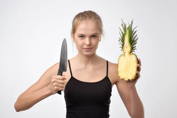 Retrato de mulher loira que mantém abacaxi e faca nas mãos contra o fundo branco — Fotografia de Stock