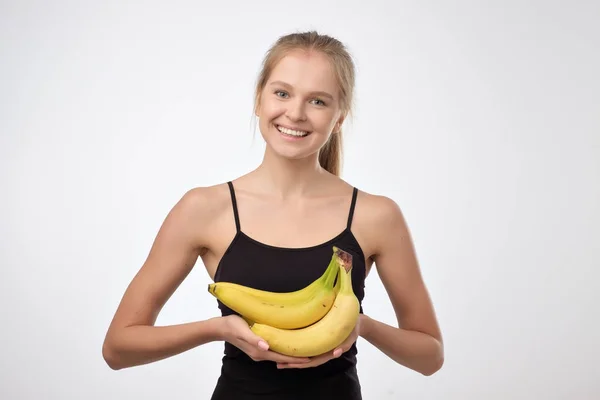 Hübsche blonde Frau mit mehreren Bananen in den Händen und einem Lächeln — Stockfoto