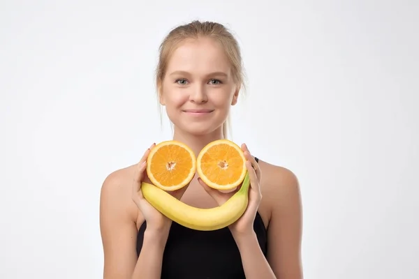 Kaukasische blonde Frau hält Banane und die Hälfte der Orangen in der Hand. — Stockfoto