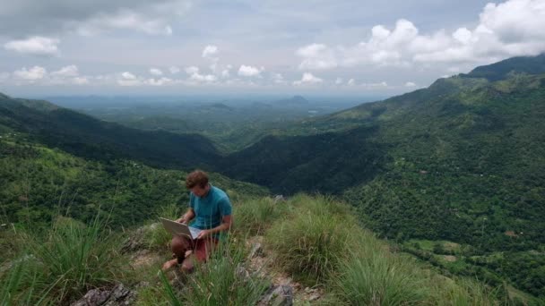 Handsome european man freelancer working on a laptop outdoors in mountains. — Stock Video